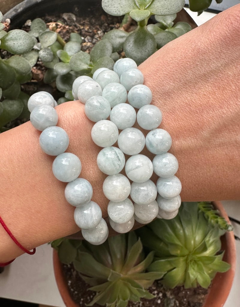 Stack of light blue beaded bracelets on a wrist with a blurred background of green plants.