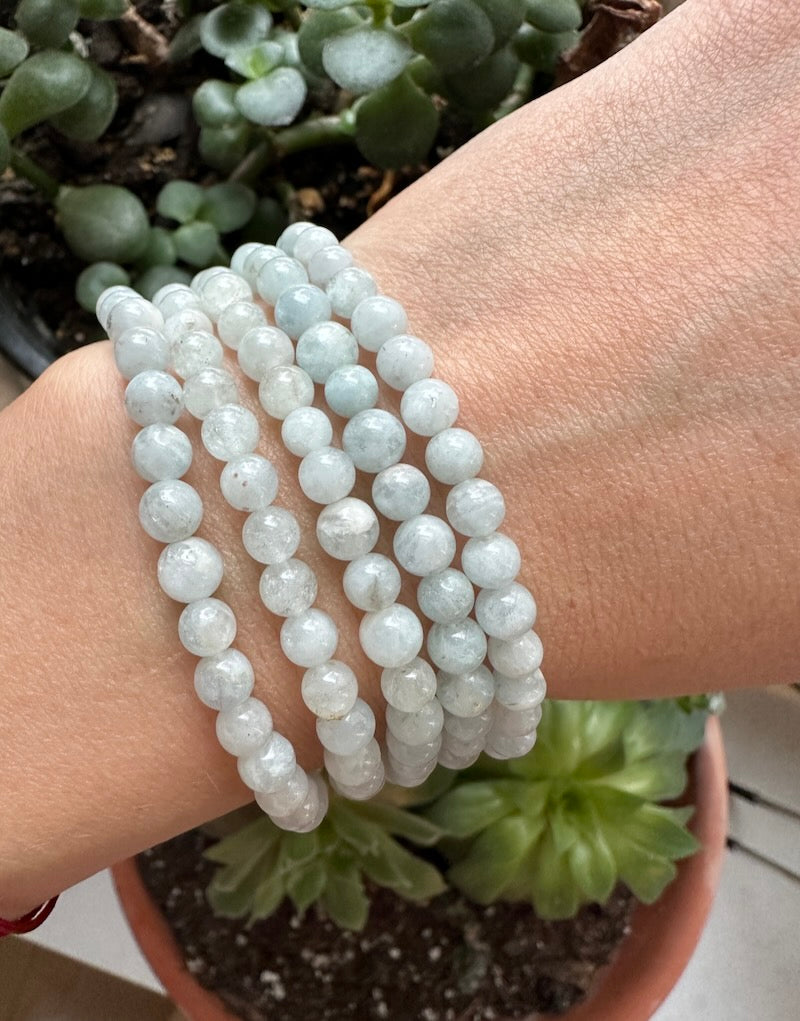 White beaded bracelets on a wrist with a plant in the background
