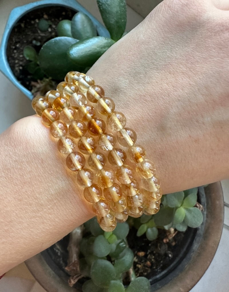 Close-up of a wrist wearing a beaded bracelet with plants in the background
