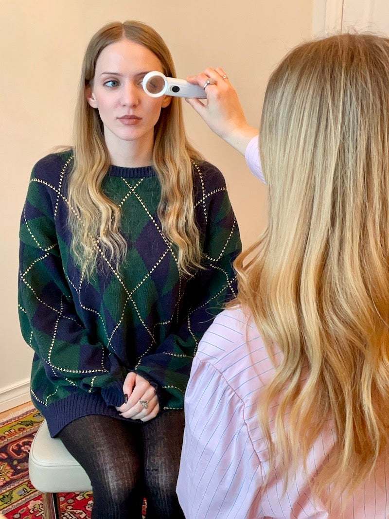 Woman in a green and navy patterned sweater being examined by a healthcare professional with a device.