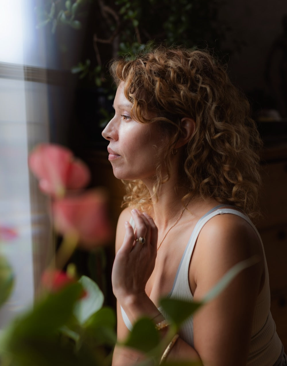 Woman wearing a white tank in a softly lit space
