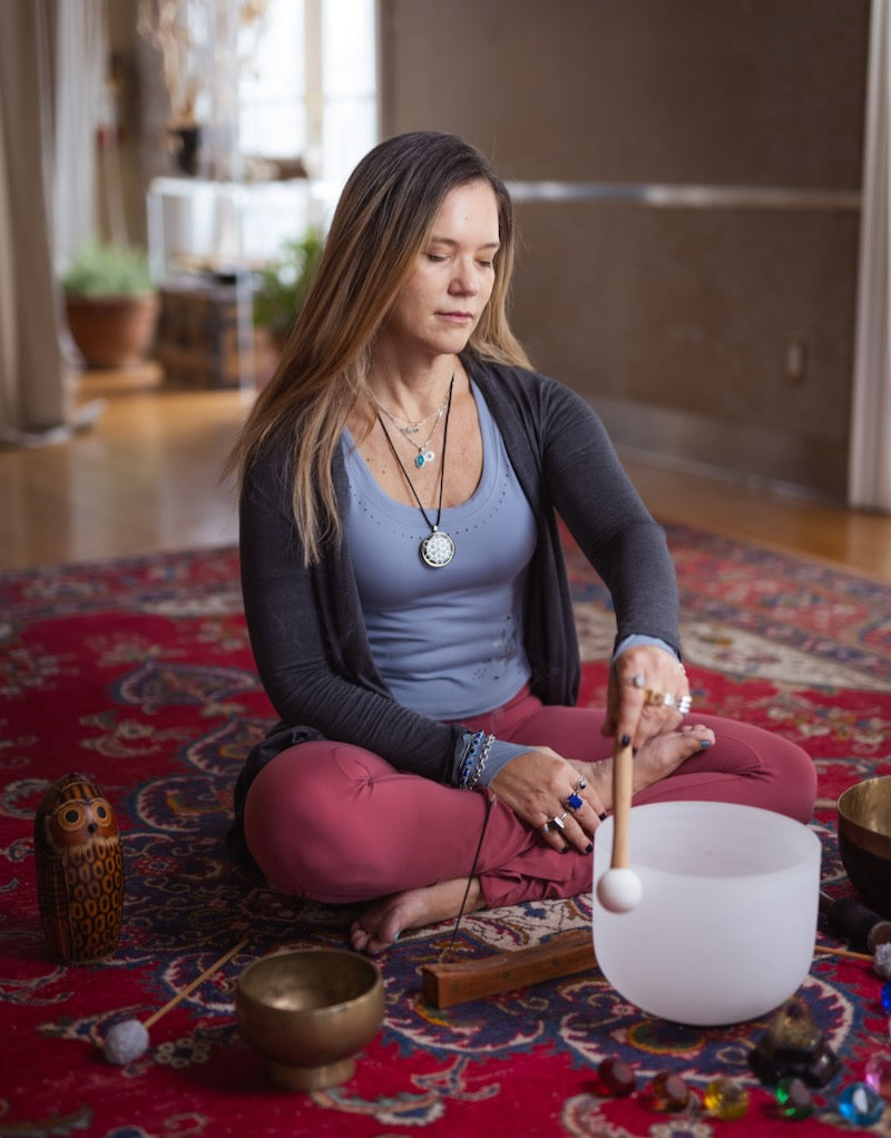 Woman meditating with a crystal singing bowl on a red rug