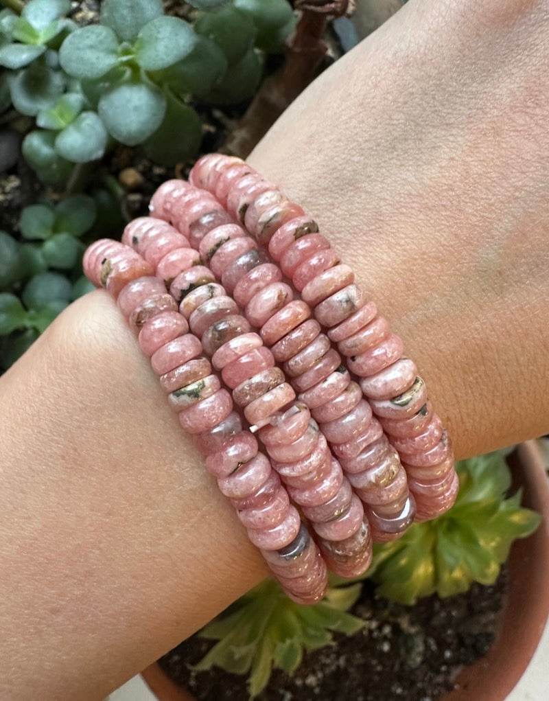 Pink beaded bracelet on a wrist with a blurred plant background