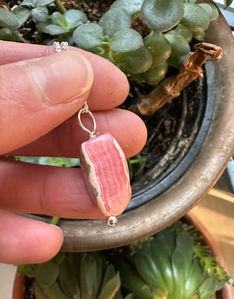 Pink stone earring held between fingers with a plant in the background